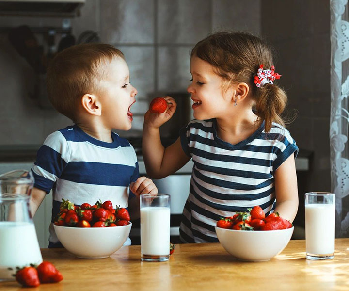 A boy and girl eating strawberries at the table