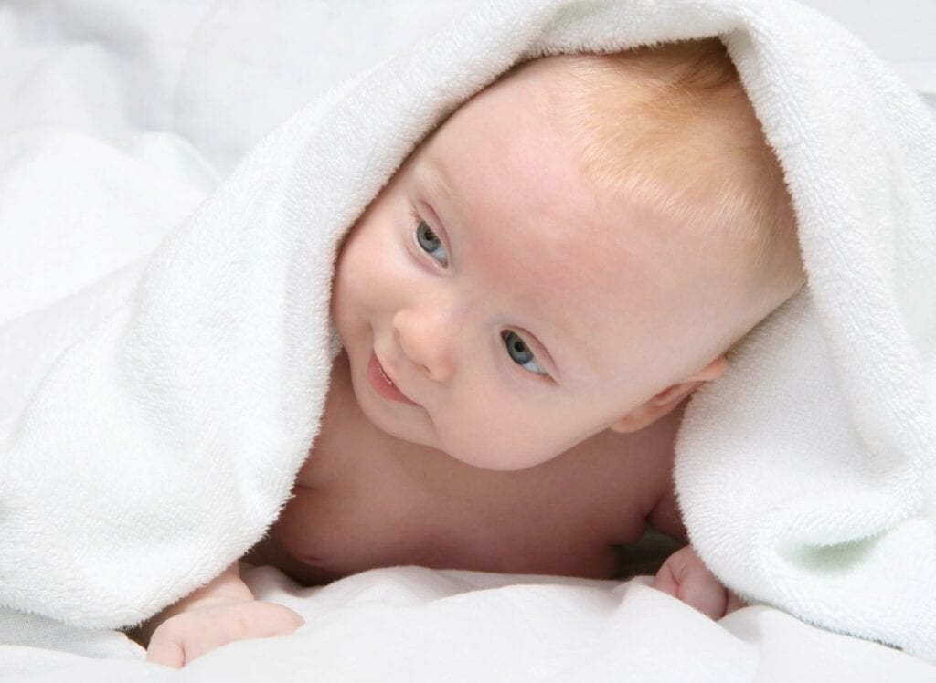 A baby is wrapped in a blanket and smiling.