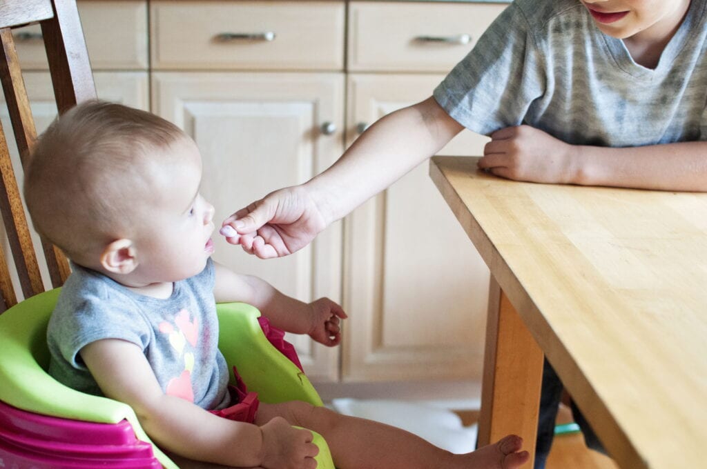 A baby in a high chair being fed by an adult.