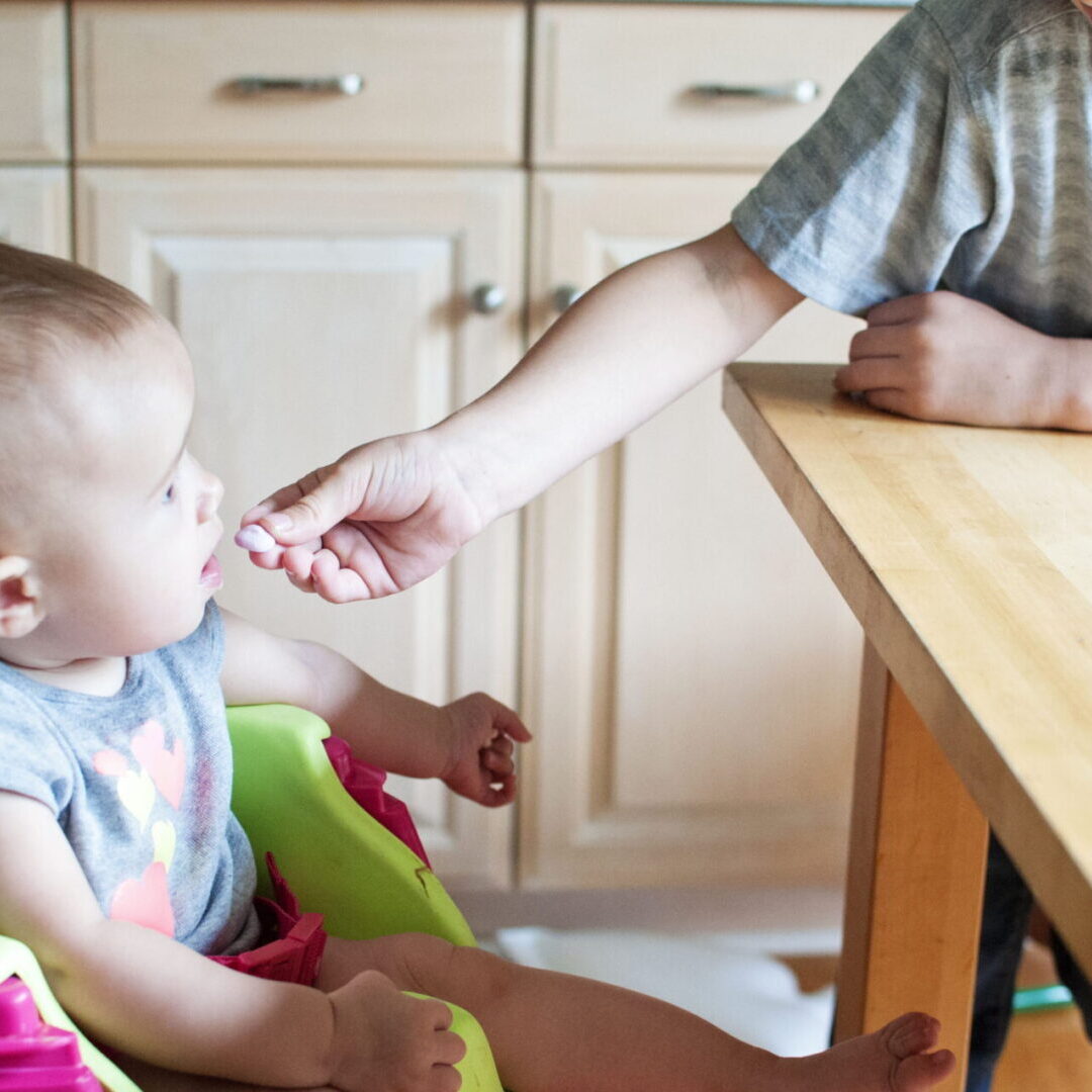 A baby in a high chair being fed by an adult.